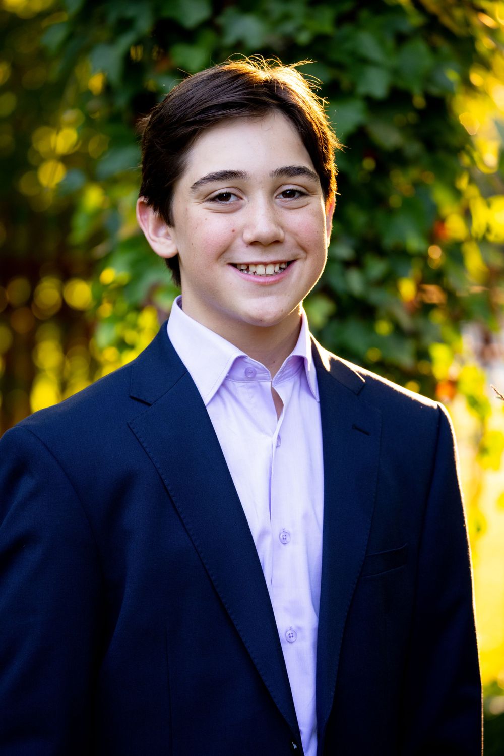 Outdoor portrait in navy suit and pink shirt with natural foliage background.