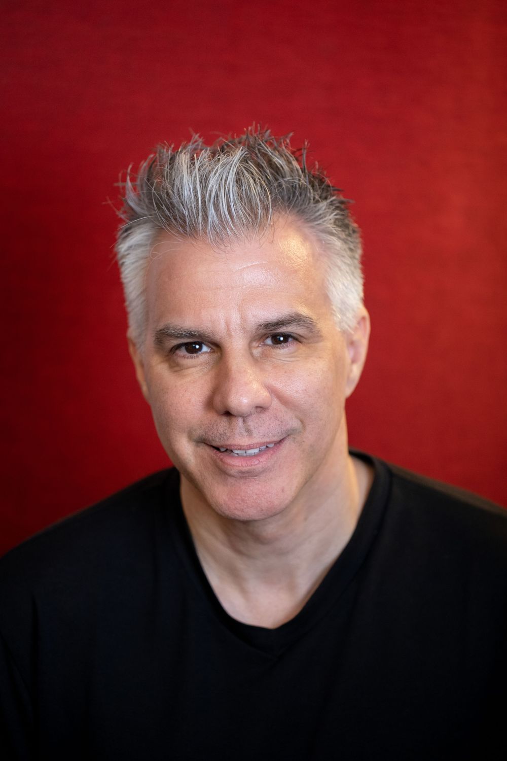 Professional headshot against red background showing person wearing black shirt.
