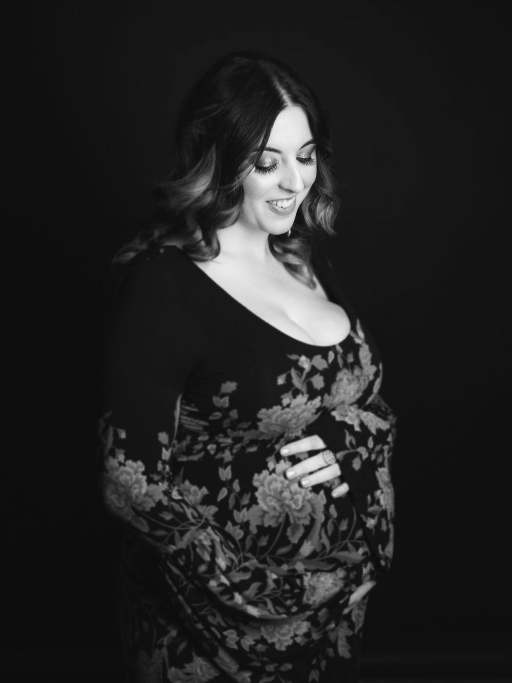 A black and white portrait of a woman in a floral dress against dark background.