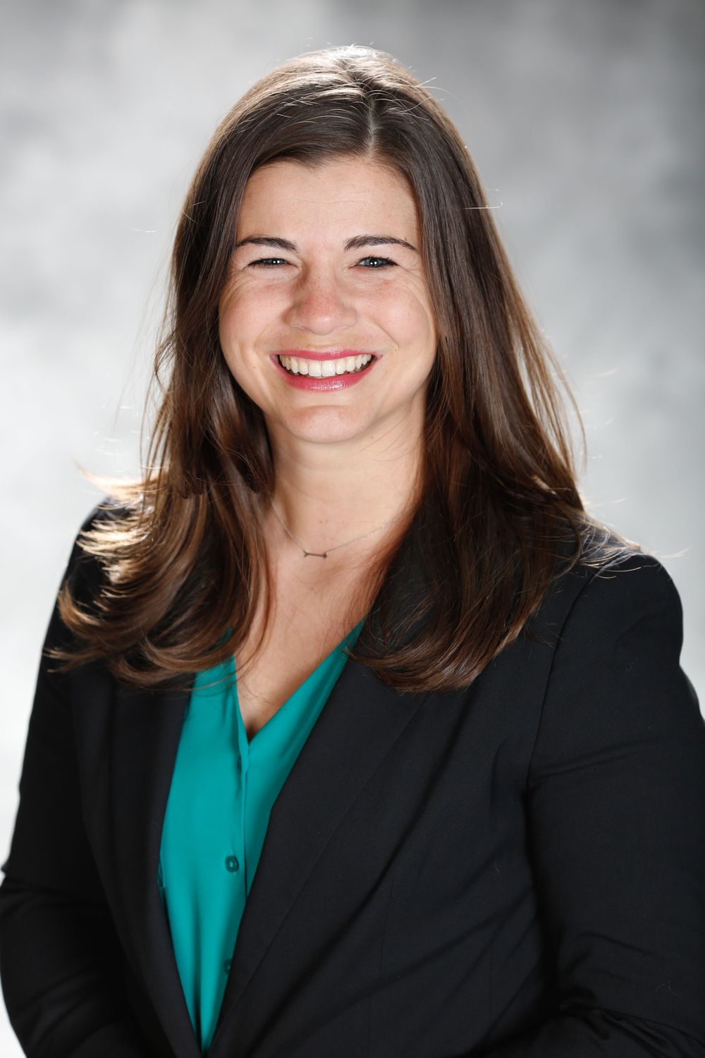 Professional headshot of a person in a black blazer and teal blouse smiling at the camera.