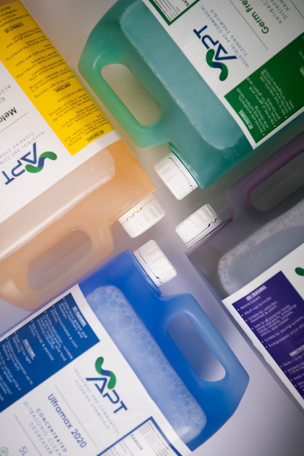 Overhead view of multiple APT brand cleaning product bottles in various colors arranged together.
