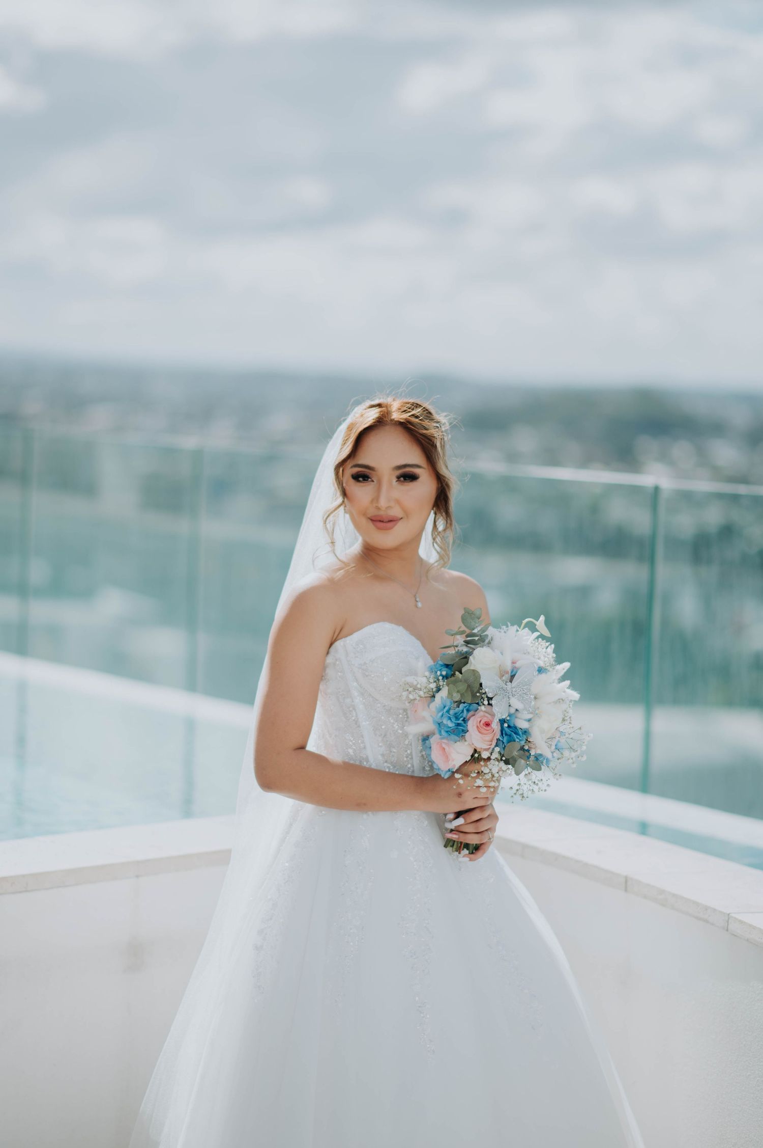 A bridal portrait on a rooftop deck with a bouquet featuring blue and pink flowers.