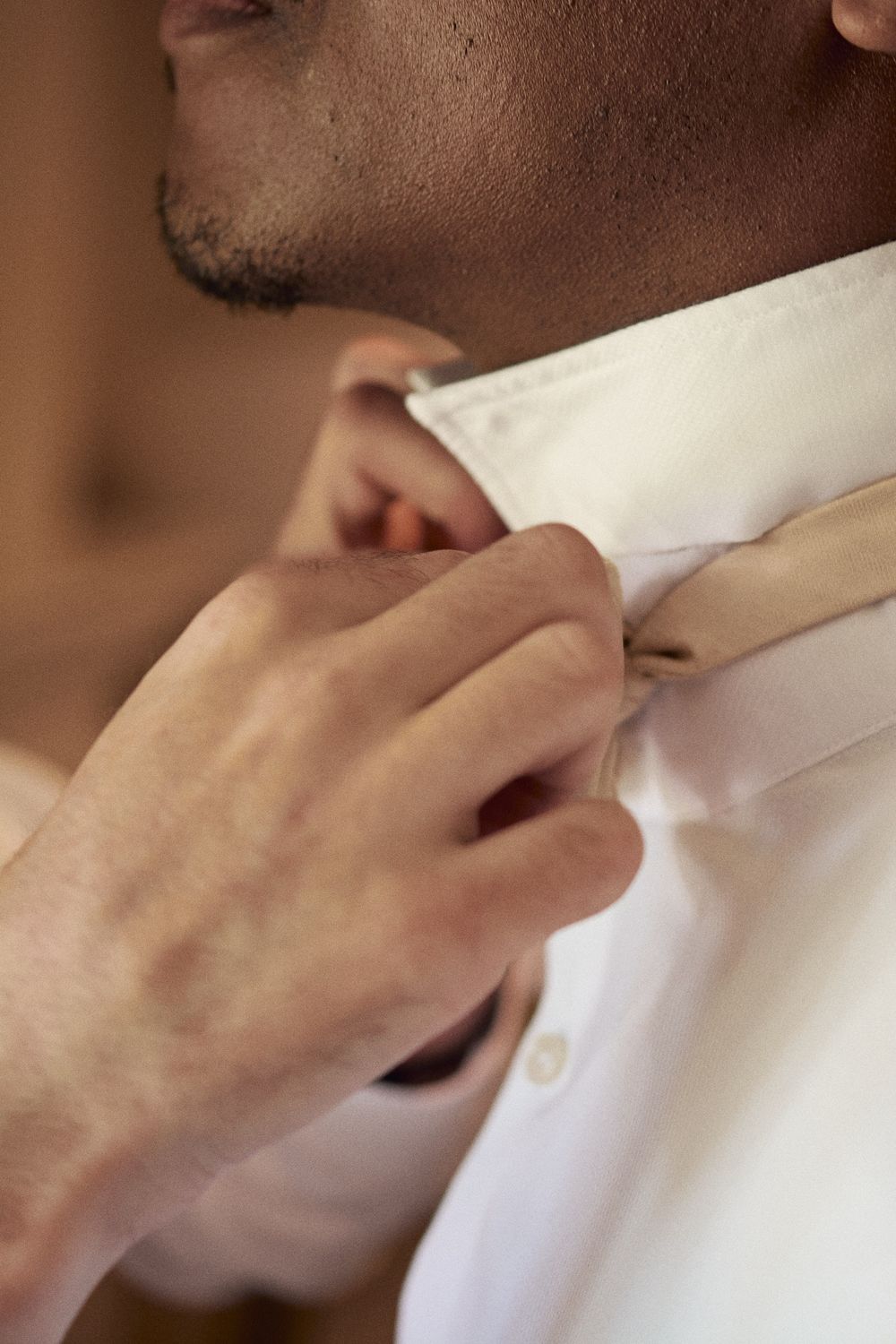 Close up of hand fixing gold bow tie around groom's neck