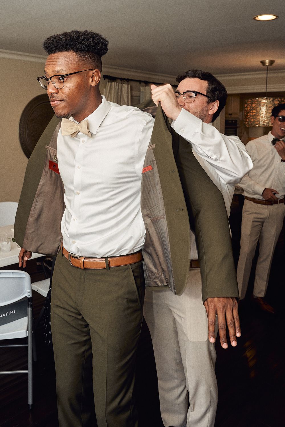 Best man helping groom put his jacket on while getting ready for his wedding day