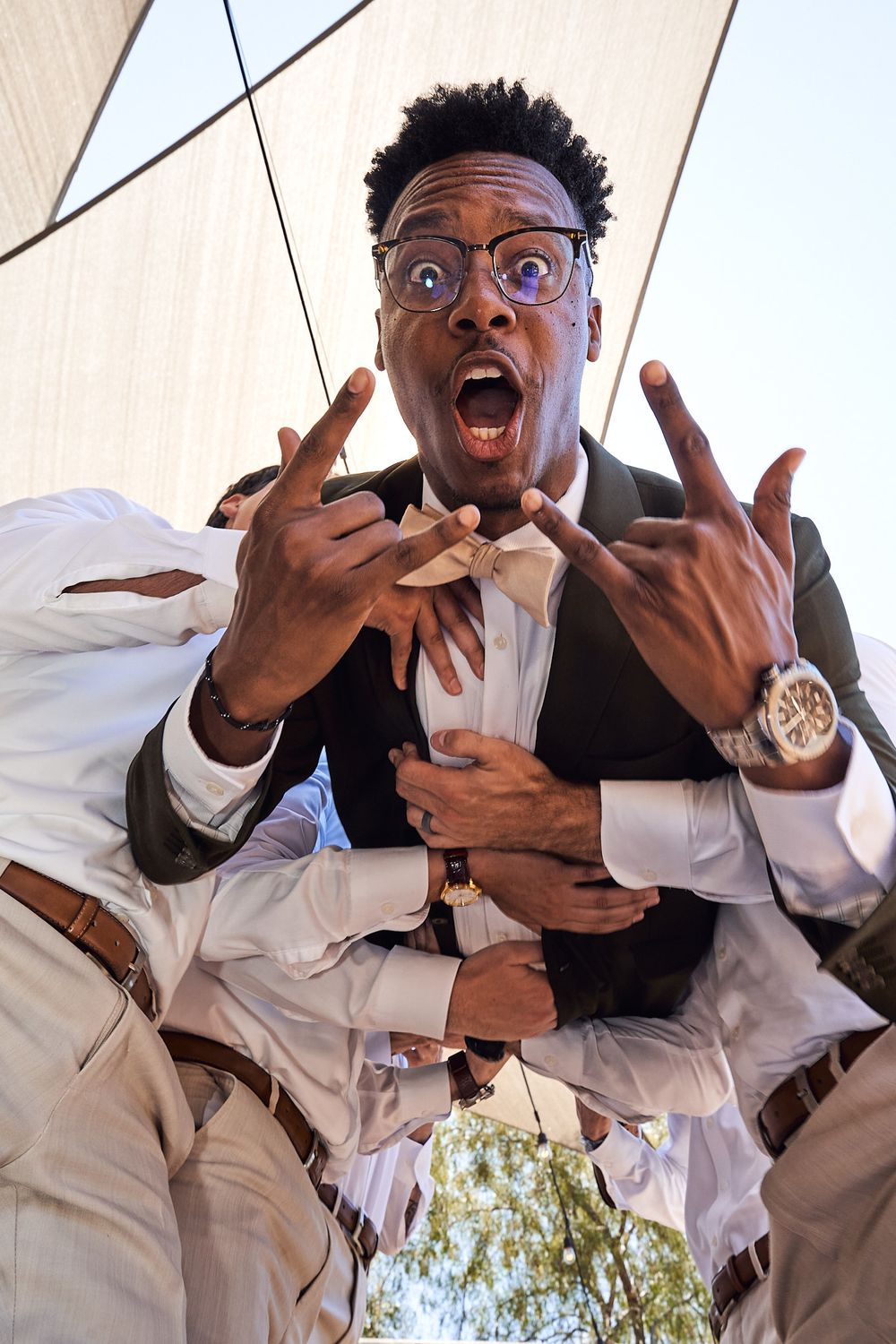 Wide low angle shot of groomsmen carrying groom as he looks excited before his wedding ceremony.