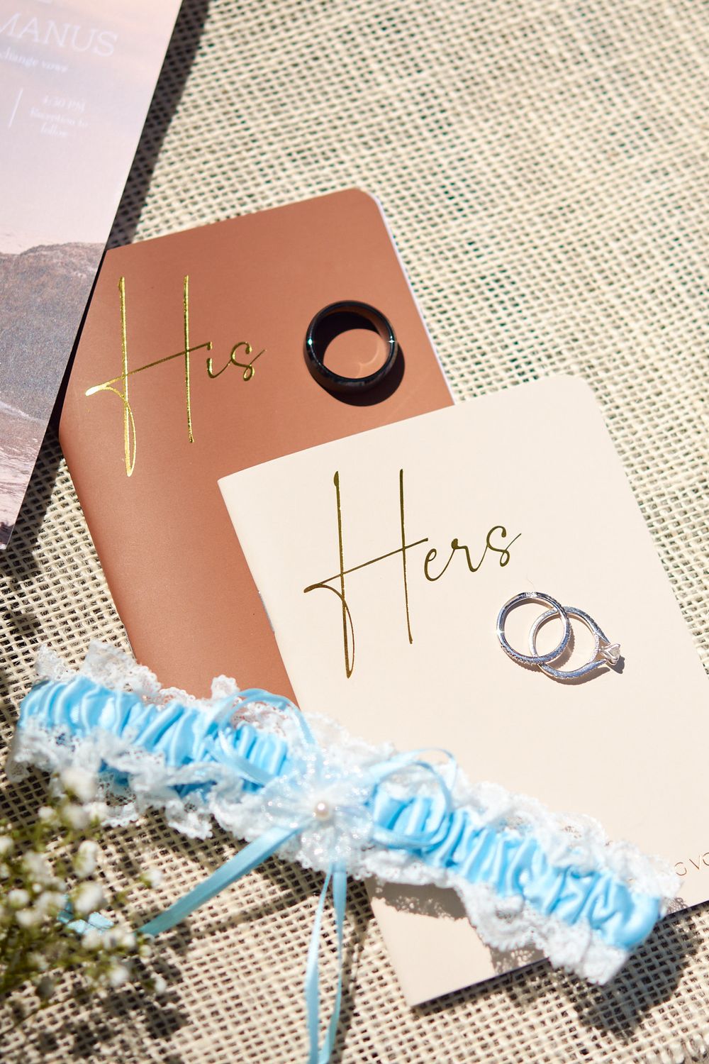 Lay flat image of wedding bands and His & Hers vow books with the bride's blue garter.