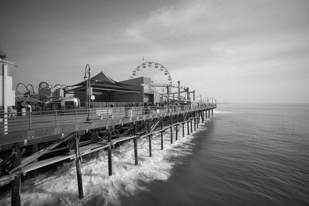 Black and white image of an oceanfront pier with Ferris wheel and amusement rides.