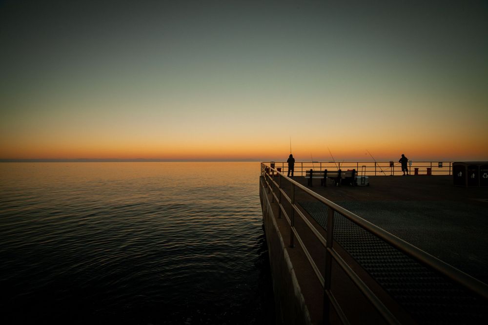 Silhouetted pier stretches into calm ocean during golden sunset.