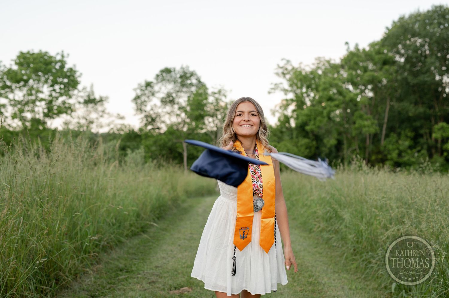 Graduate celebrates with cap toss in field during outdoor graduation photoshoot.