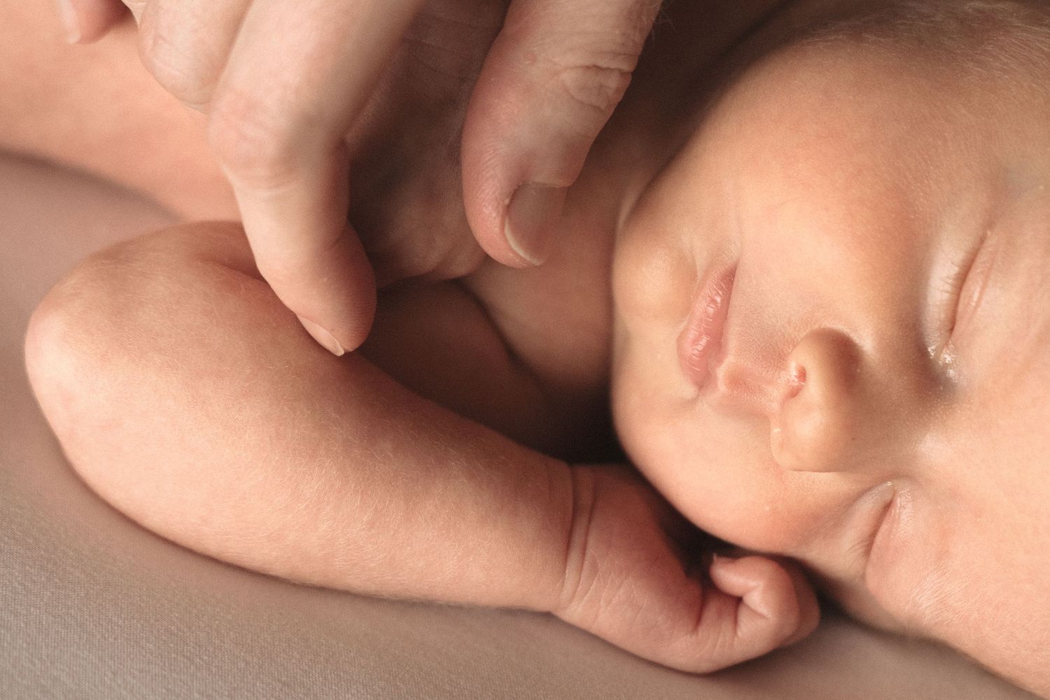 A sleeping baby with peaceful expression rests with tiny fingers curled near their face.