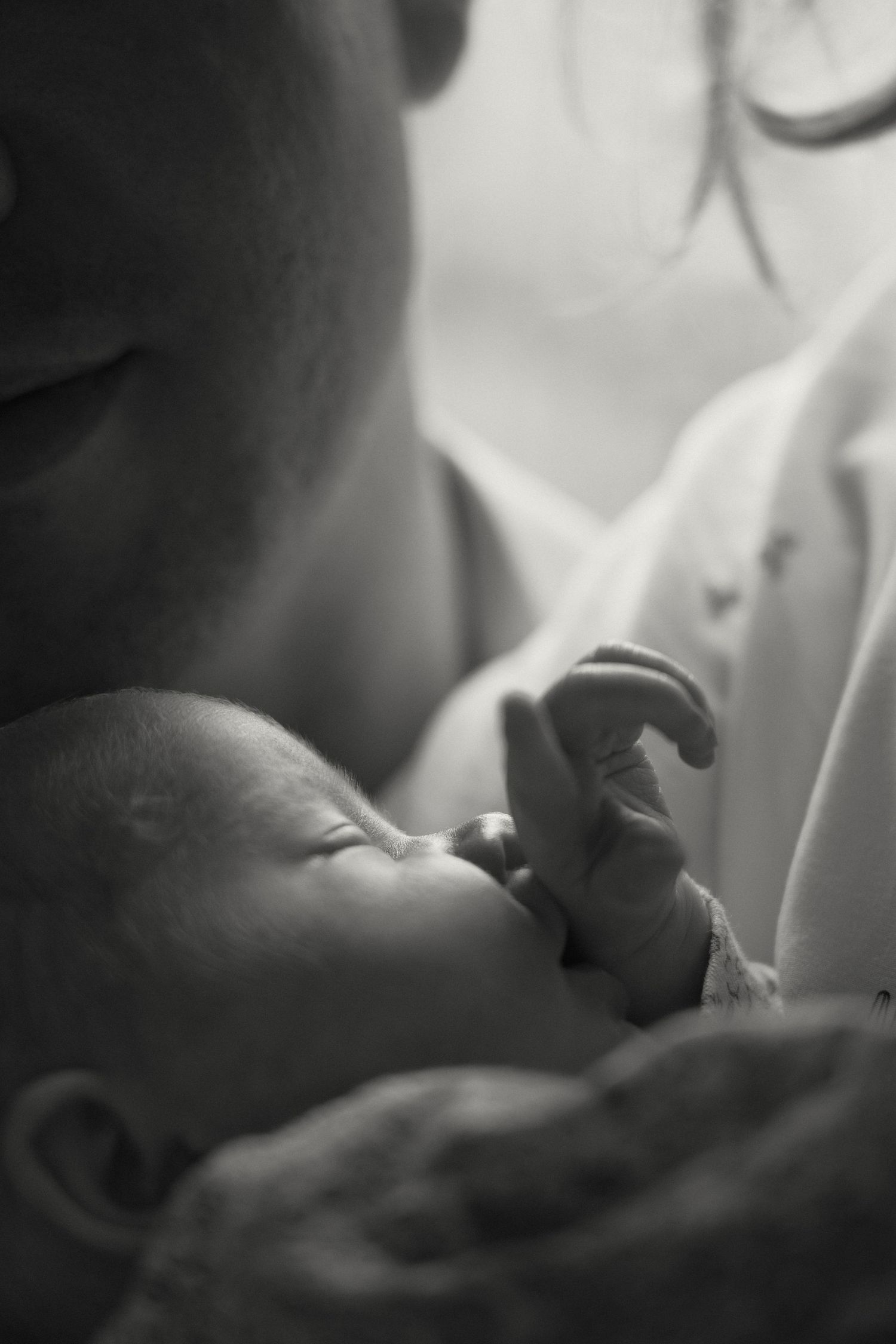 Close-up black and white photo of a sleeping newborn baby's tiny hand and face in soft focus.