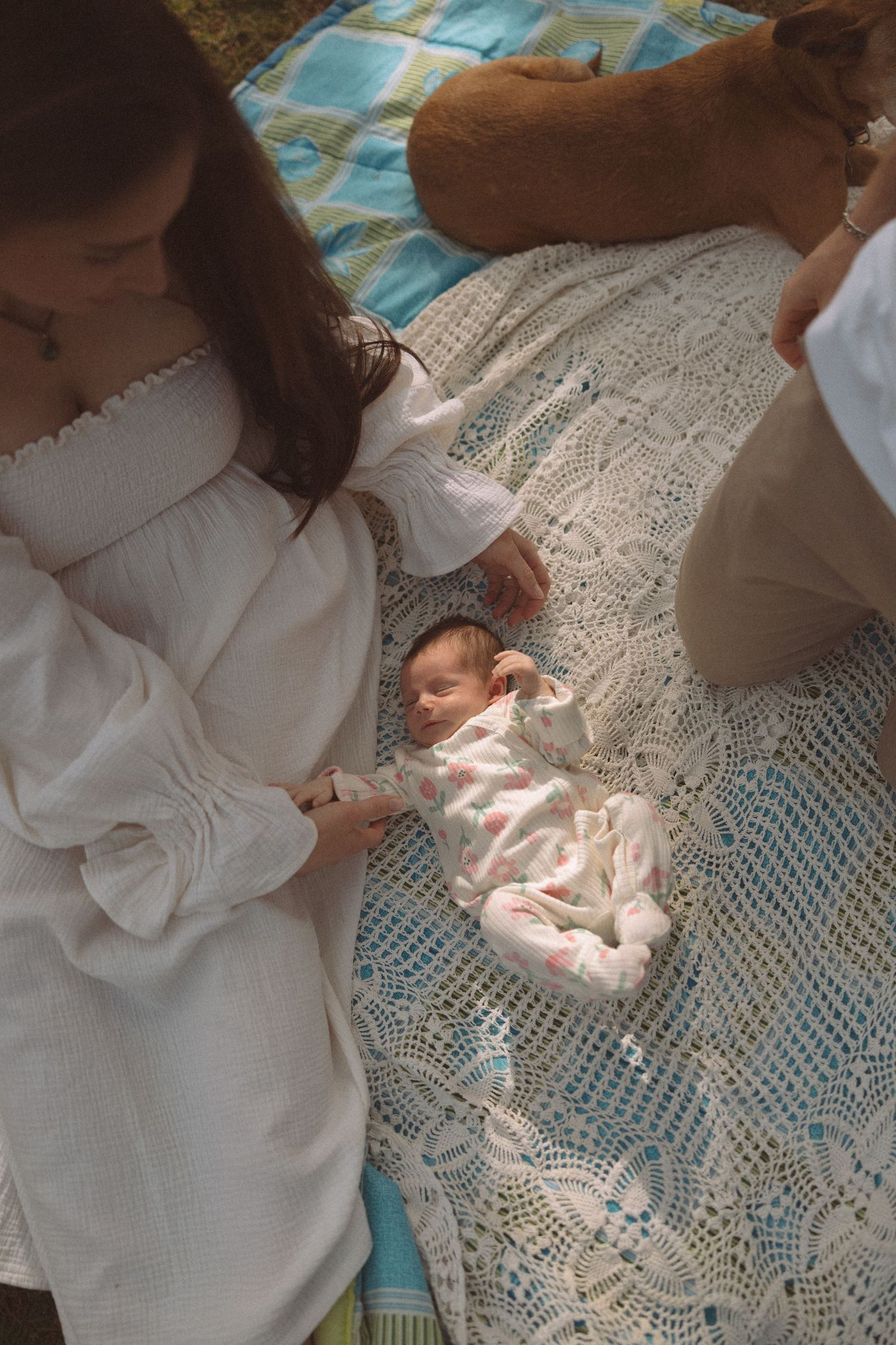 A series of photos showing someone in a white dress gently interacting with a small baby on a lace blanket.