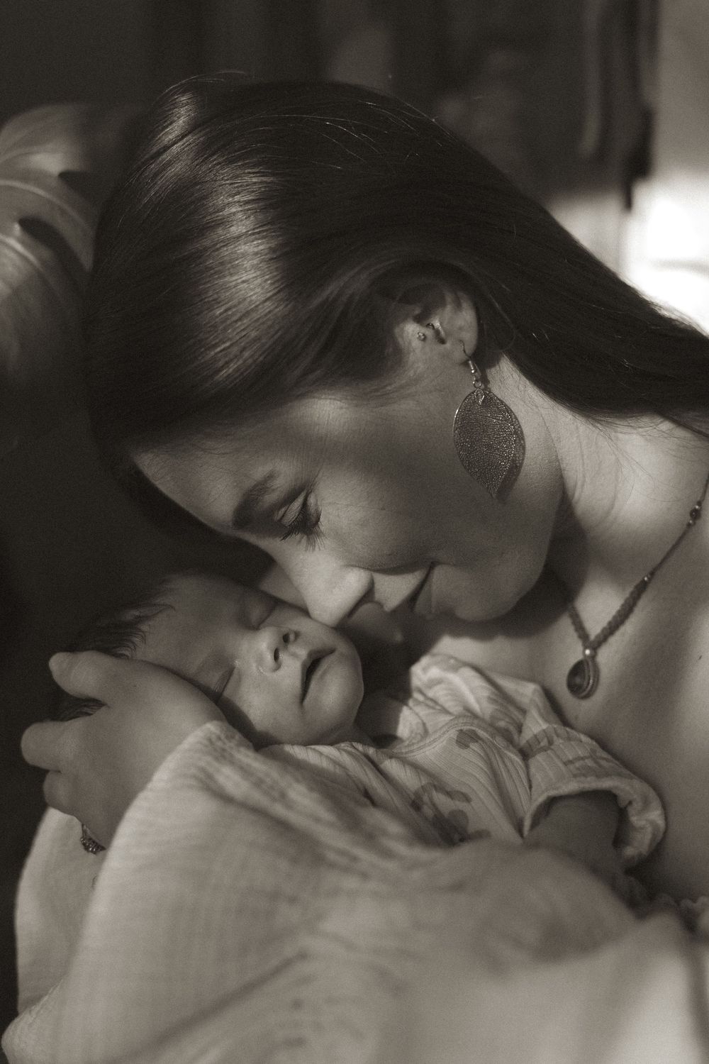 A tender black and white photo sequence showing a mother gently kissing and bonding with her newborn baby.