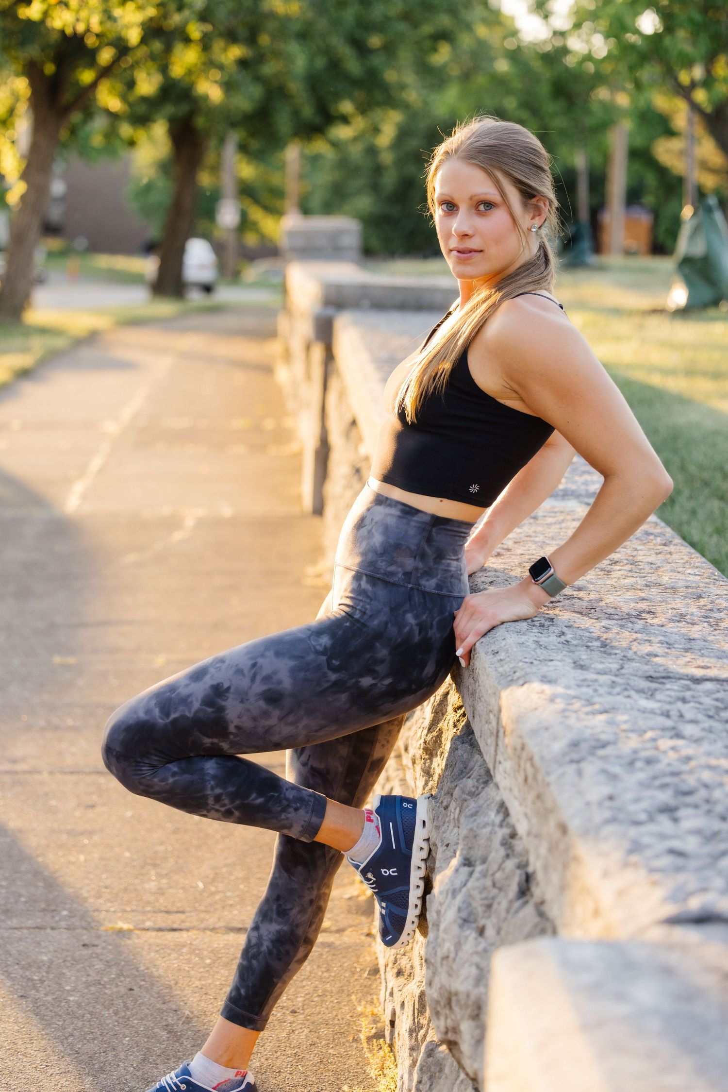 Athletic figure in patterned leggings leans against stone wall during sunset workout.