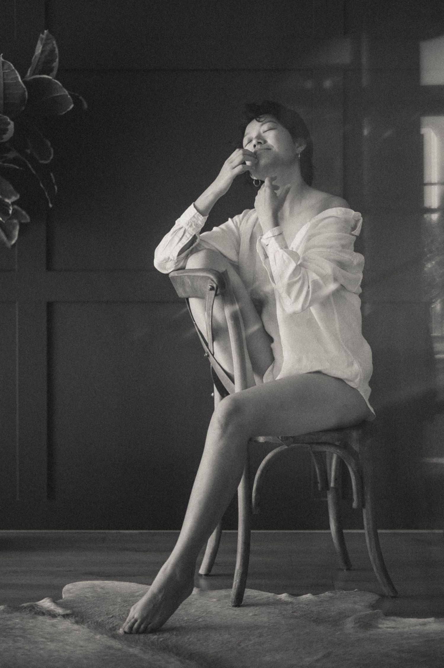 Black-and-white sensual photo in the studio: a woman sitting on a chair in a white shirt.