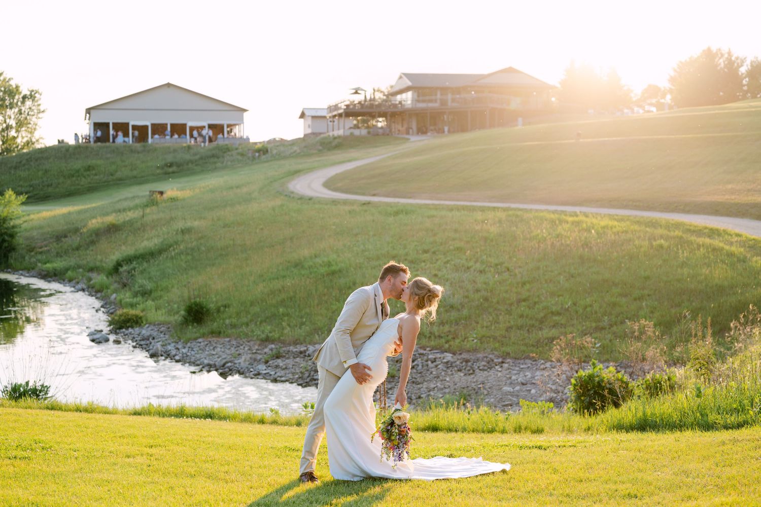 Wedding party members stand together on green lawn in front of classic white building.