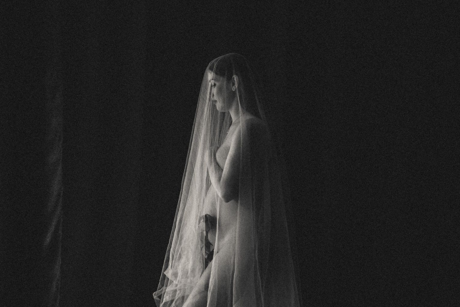 A glowing mother-to-be posing in a professional studio with dramatic lighting and soft drapery.