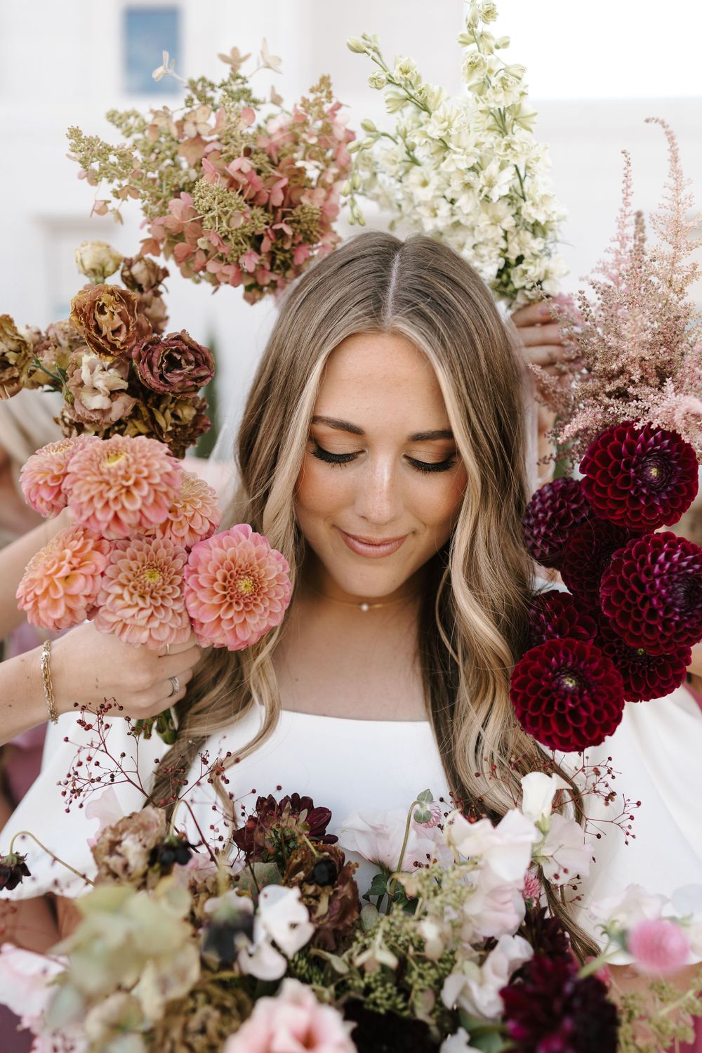 Beautiful floral arrangement with burgundy dahlias, pink roses, and white blooms frames a close-up portrait.
