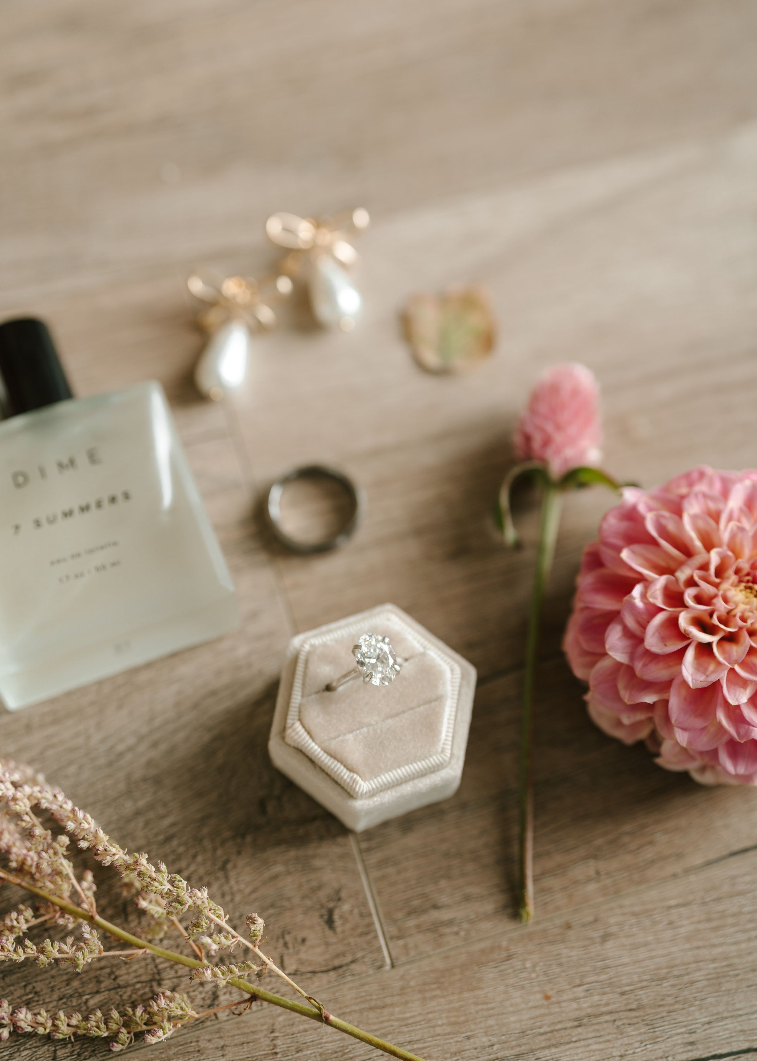 Wedding details flatlay with pearl earrings, perfume, rings and pink dahlia flower.