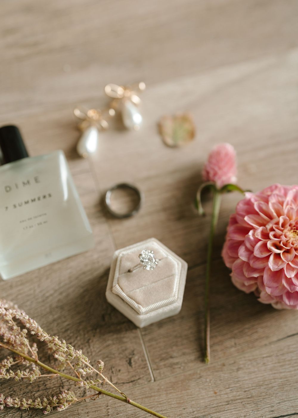 Wedding details flatlay with pearl earrings, perfume, rings and pink dahlia flower.