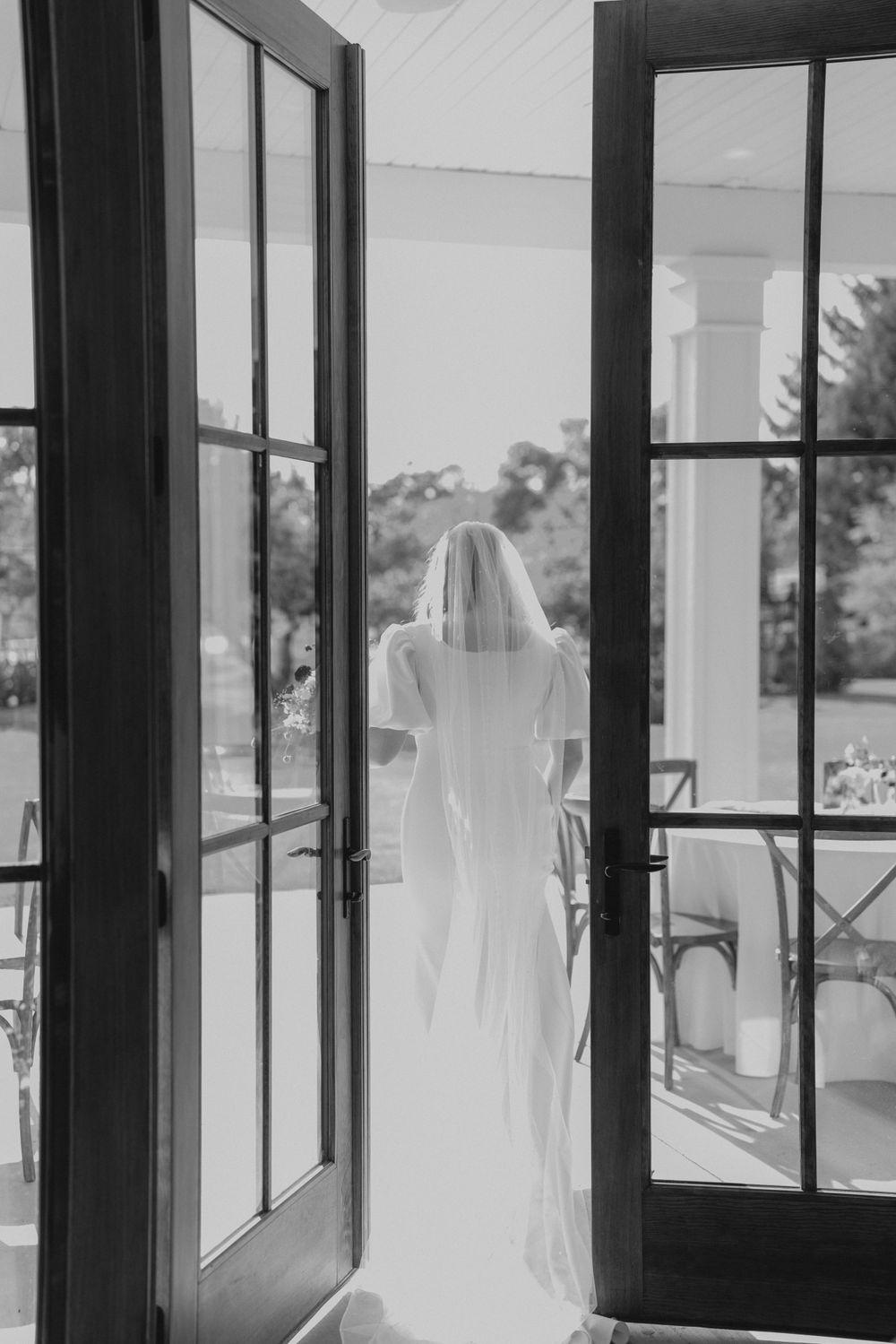 Silhouette of a person in flowing white dress and veil looking out French doors.
