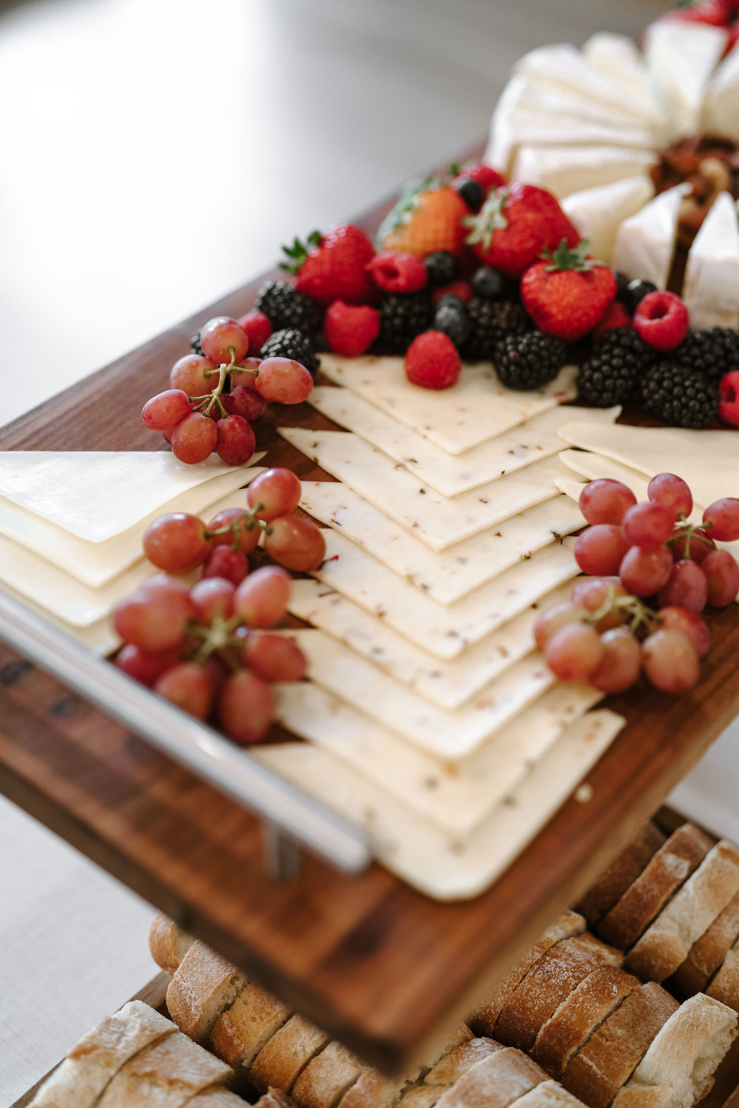 Gourmet cheese board decorated with fresh berries and grapes on wooden serving platter.