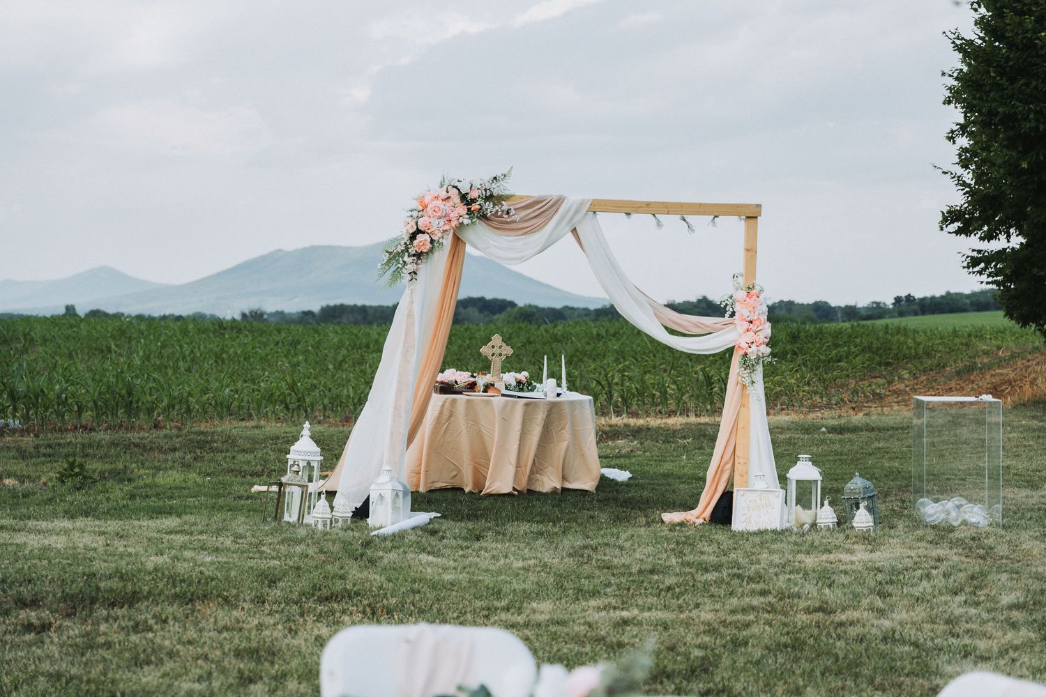 Rustic wedding arch with flowing white fabric and floral decorations in mountain setting.