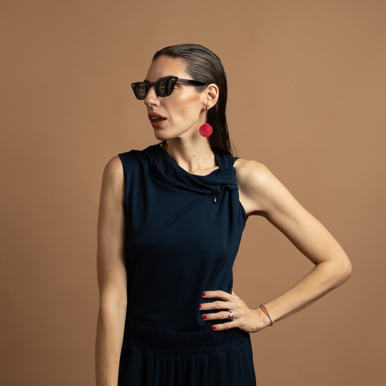Professional fashion portrait against brown background featuring a sleek navy dress and red statement earrings.