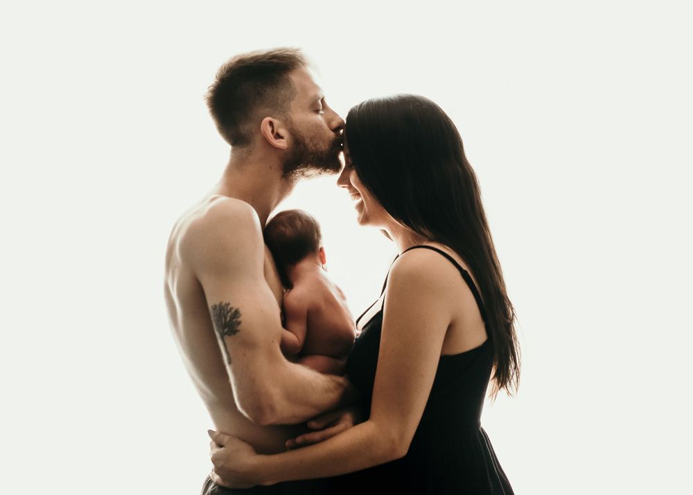 Intimate family portrait of parents sharing tender moment with newborn.