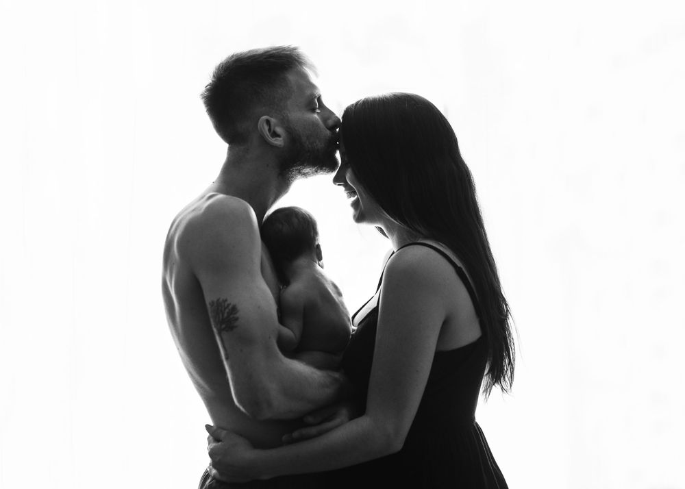 Silhouette of family embracing with newborn baby against white background.