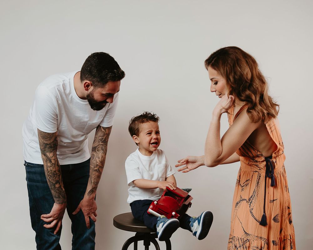 Candid family moment showing joyful interaction with child on toy tricycle.
