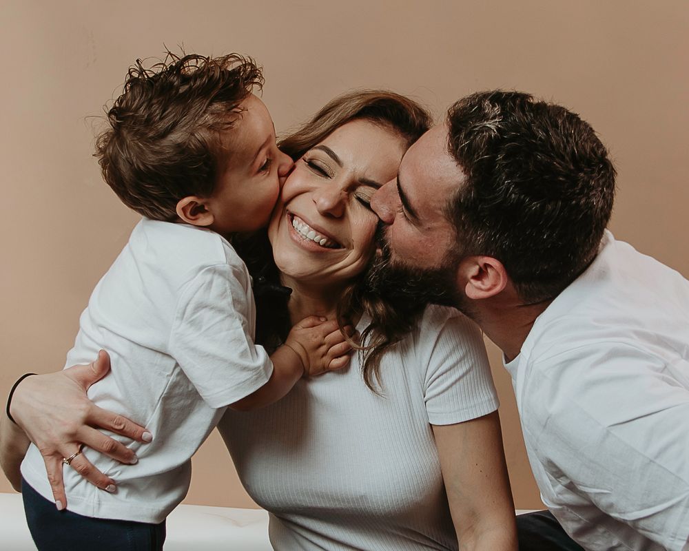 A tender family portrait with parents and toddler sharing kisses and laughter.