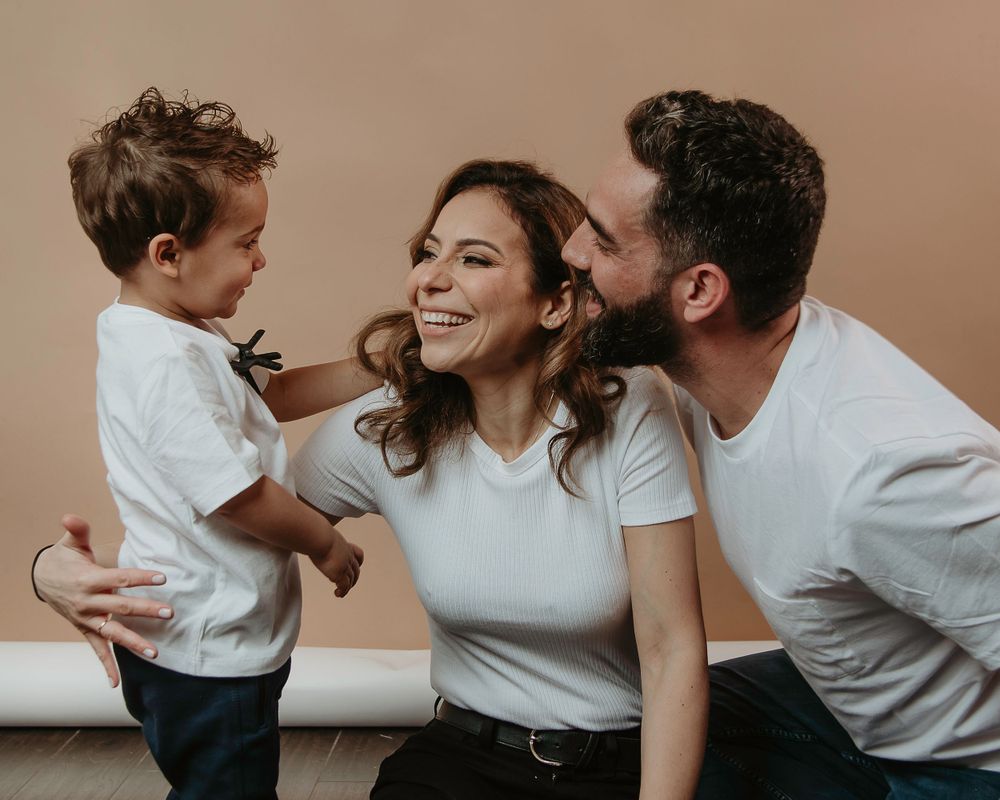 A young family sharing a joyful candid moment together against a neutral background.