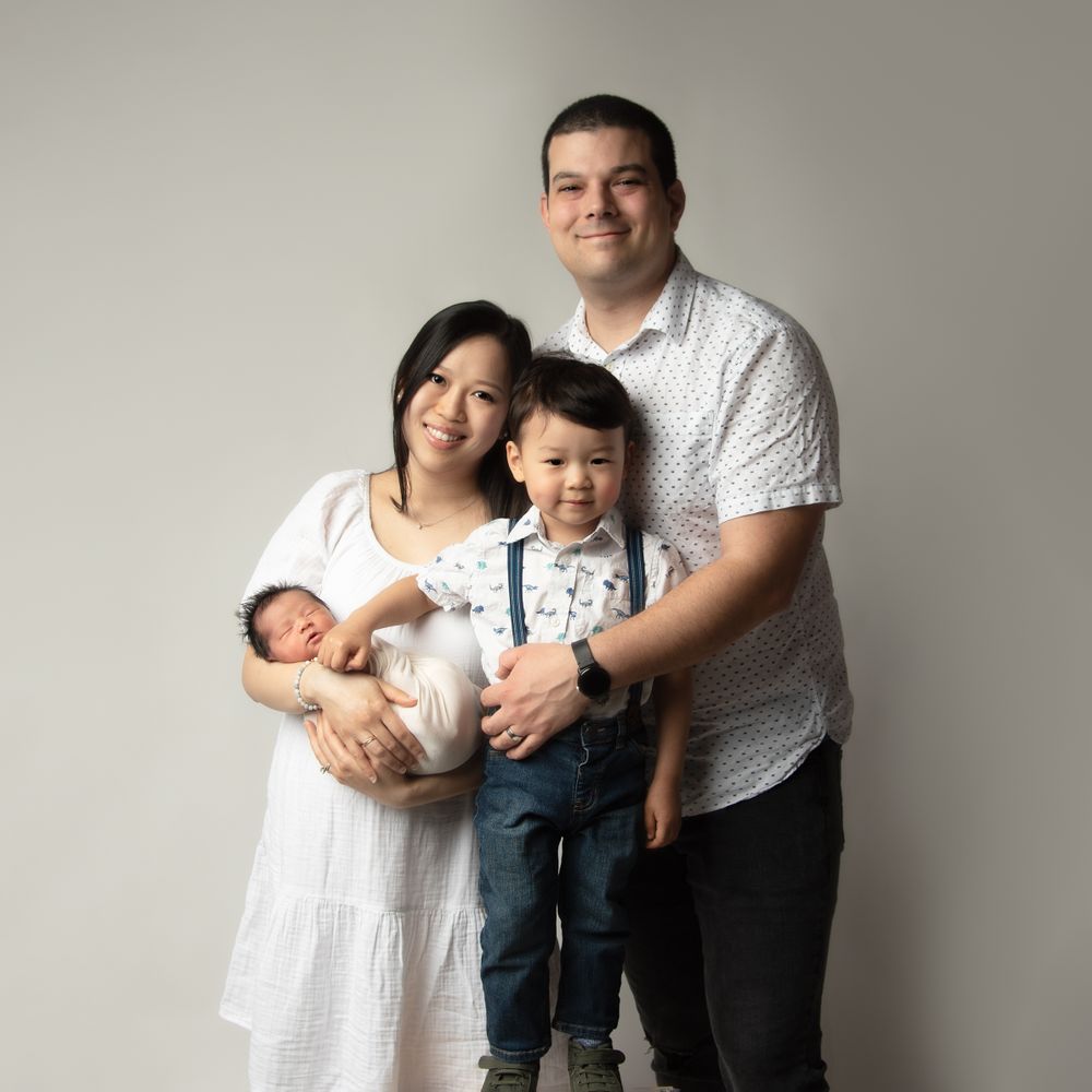A studio portrait of a young family with a newborn baby and toddler against a light backdrop.