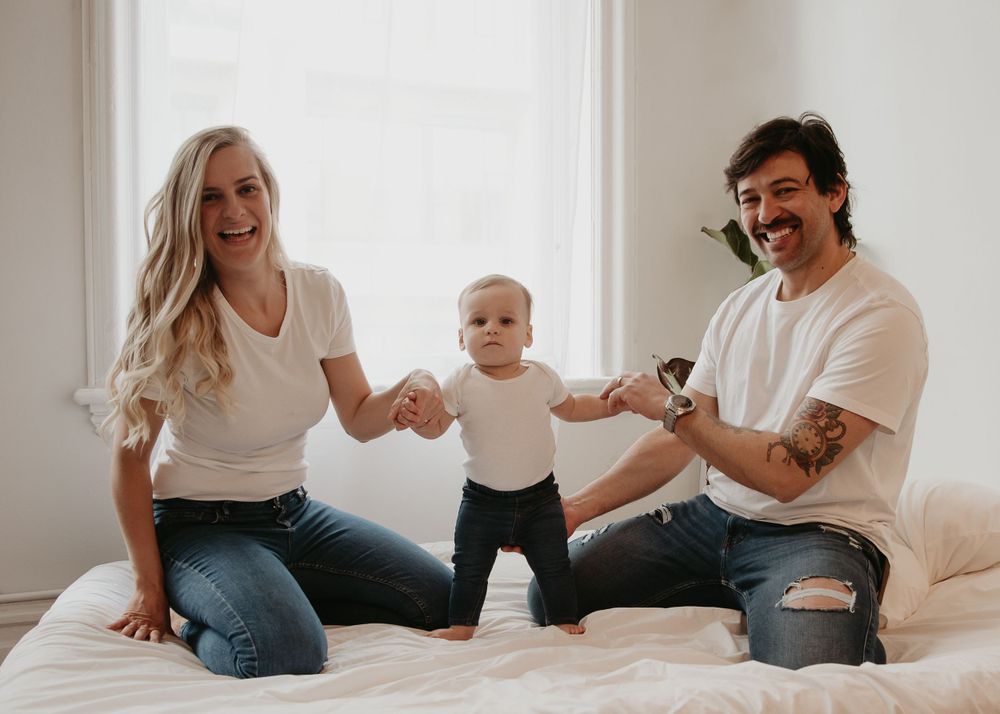 A family playing with their baby on a white bed in a bright room.