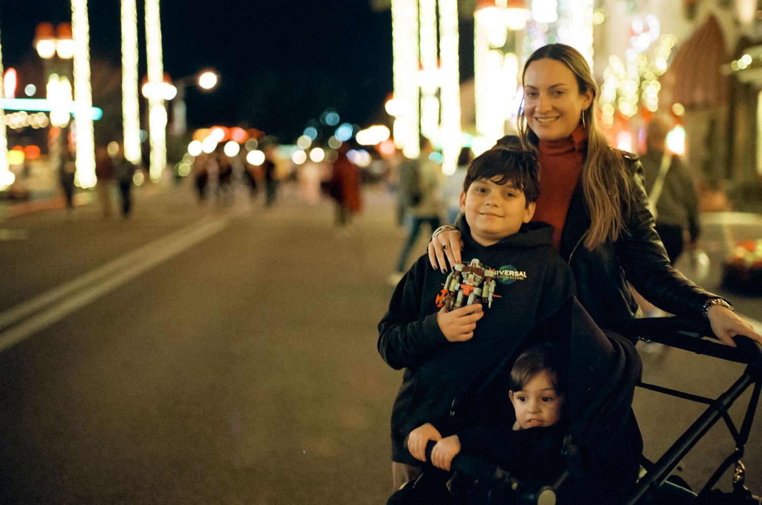 A family enjoys an evening stroll along a brightly lit street during the holiday season.