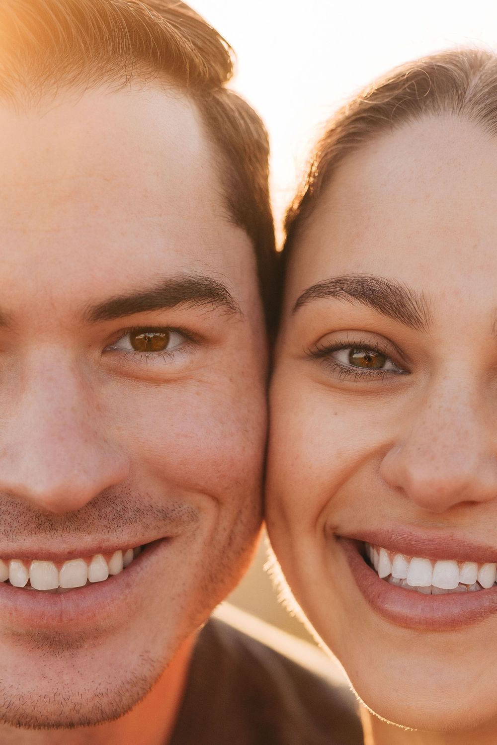 Close up portrait of couple smiling with bright white teeth against warm sunlit background.