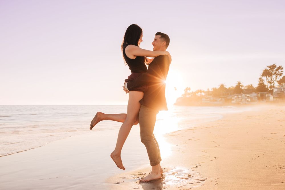 A couple shares a romantic moment on the beach at sunset, silhouetted against the golden light.