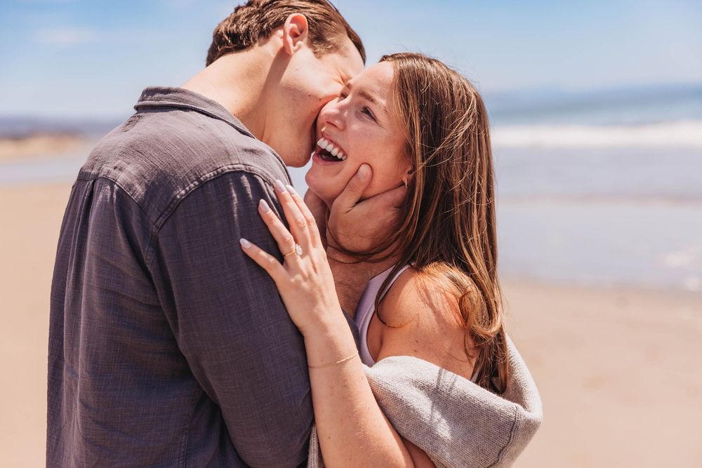 A happy engaged couple sharing a joyful intimate moment together on a sunny beach.