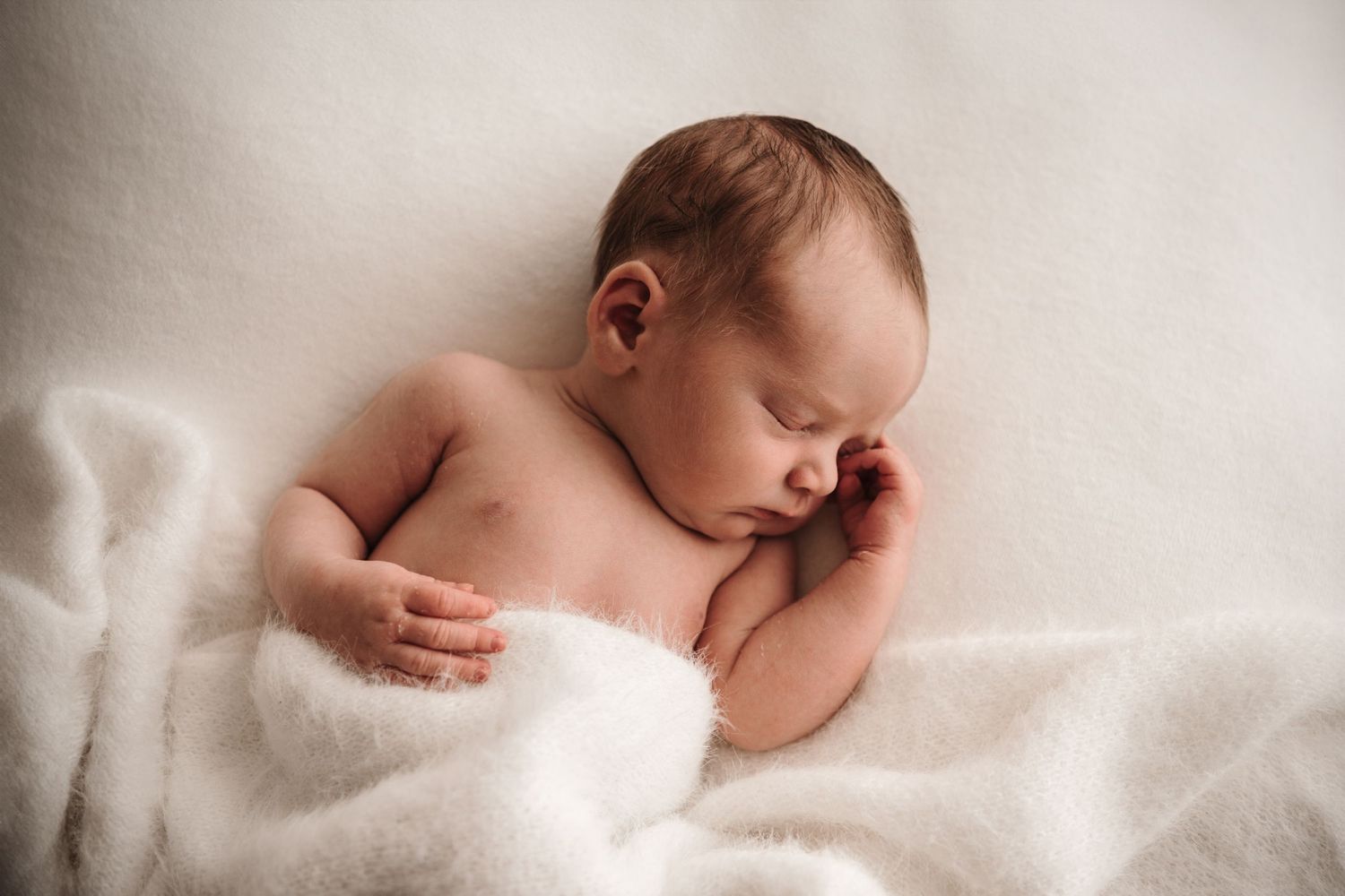 A peaceful newborn baby sleeping under a soft white blanket.