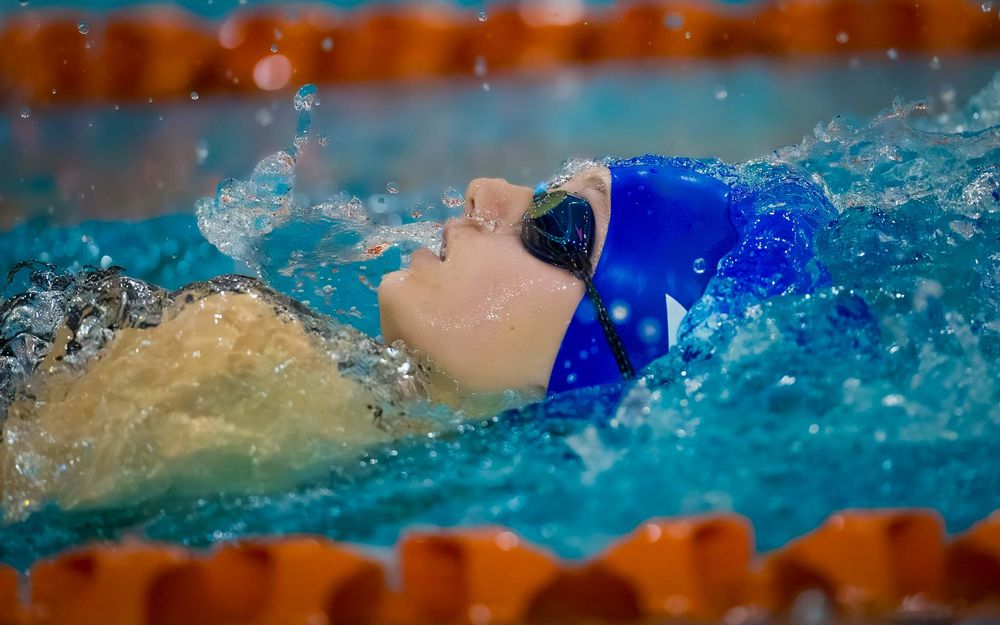 Lower Dauphin swimmer in blue cap racing backstroke during Senior Night celebration.