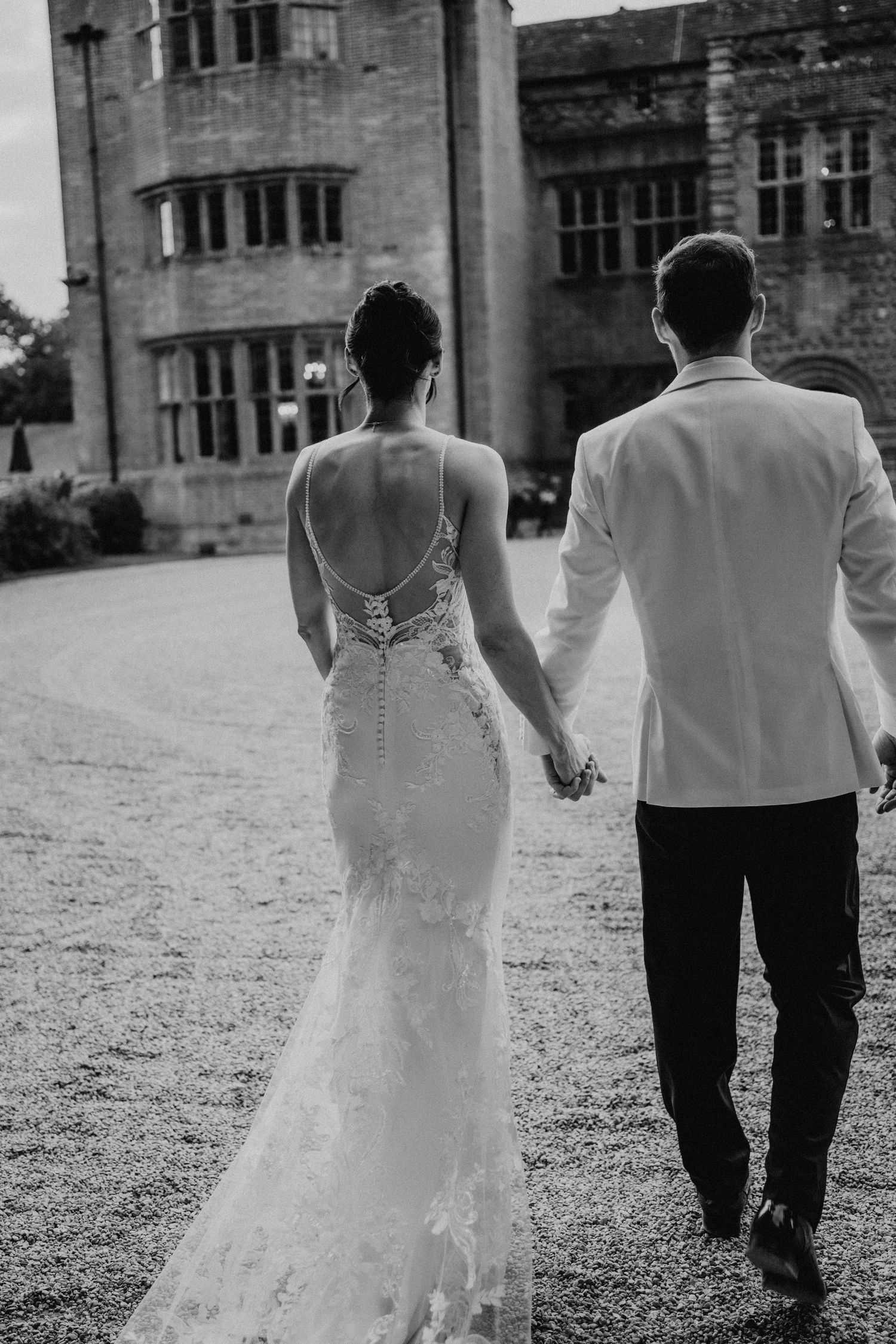 Black and white series of a couple walking away from camera at a stone castle venue in elegant wedding attire.