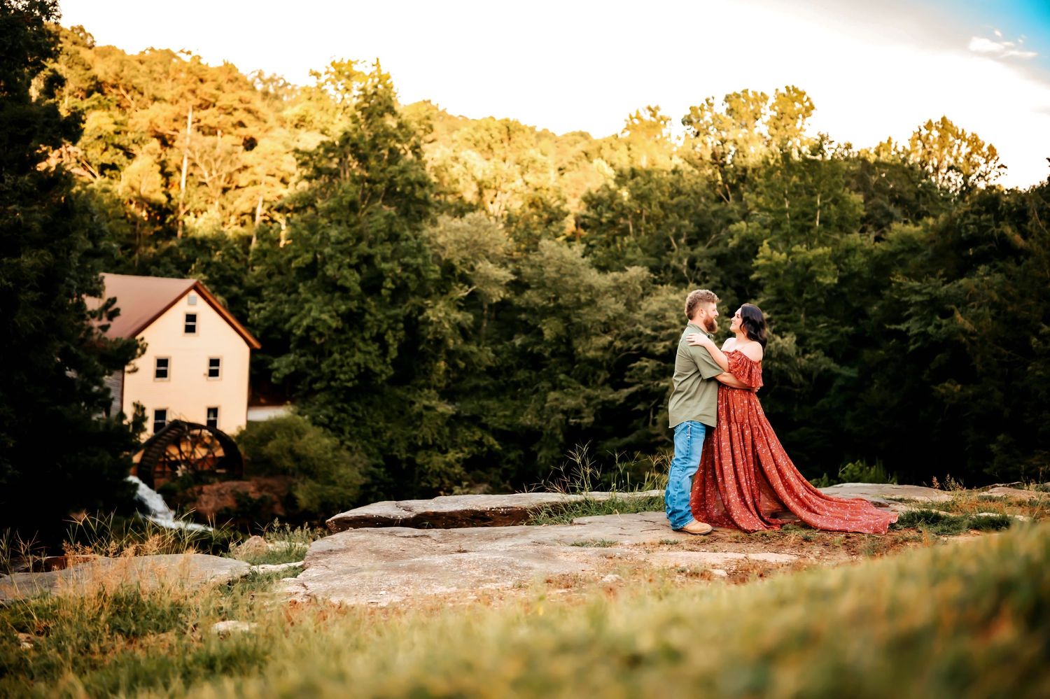 A couple shares a romantic moment in a scenic outdoor setting with golden sunlight and natural surroundings.