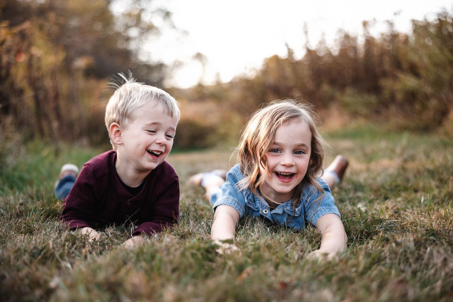 Children lying in autumn grass during golden hour outdoor photo session.