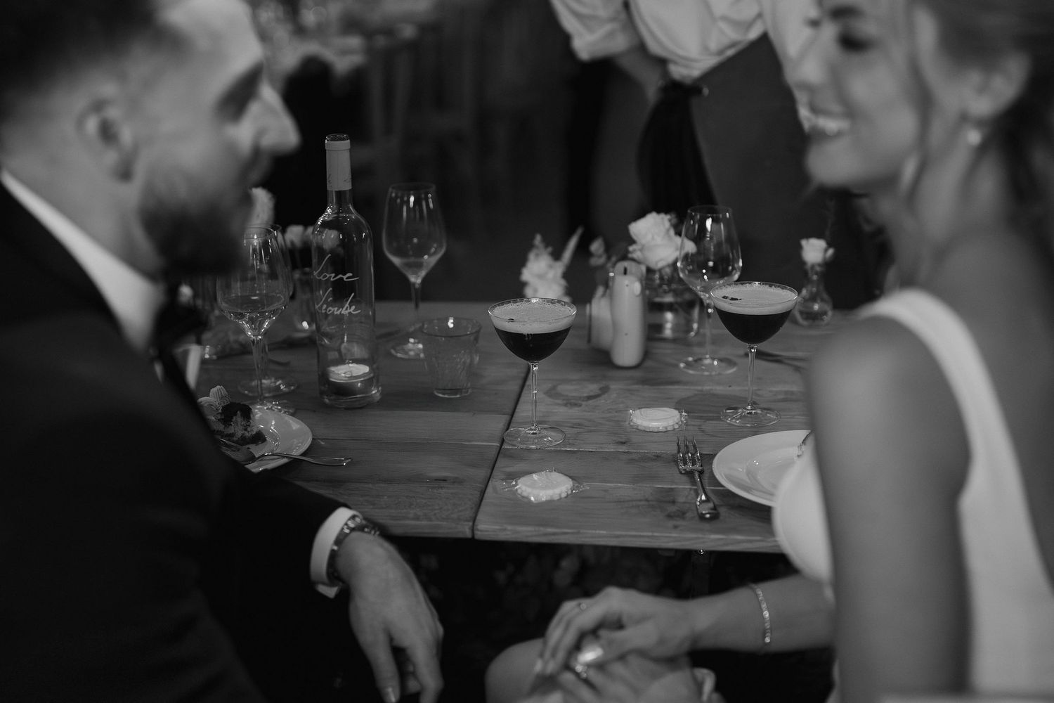 espresso martini cocktails with bride and groom sat, smiling at each other and holding hands at ivy lodge wedding in cirencester