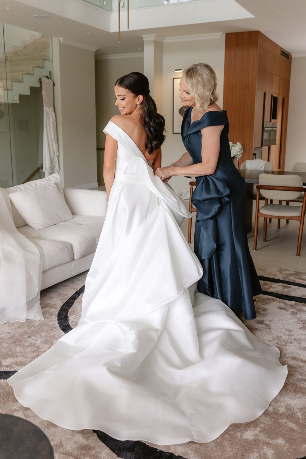 Series of photos showing bride getting dressed in flowing white wedding gown with help from attendant in navy dress.