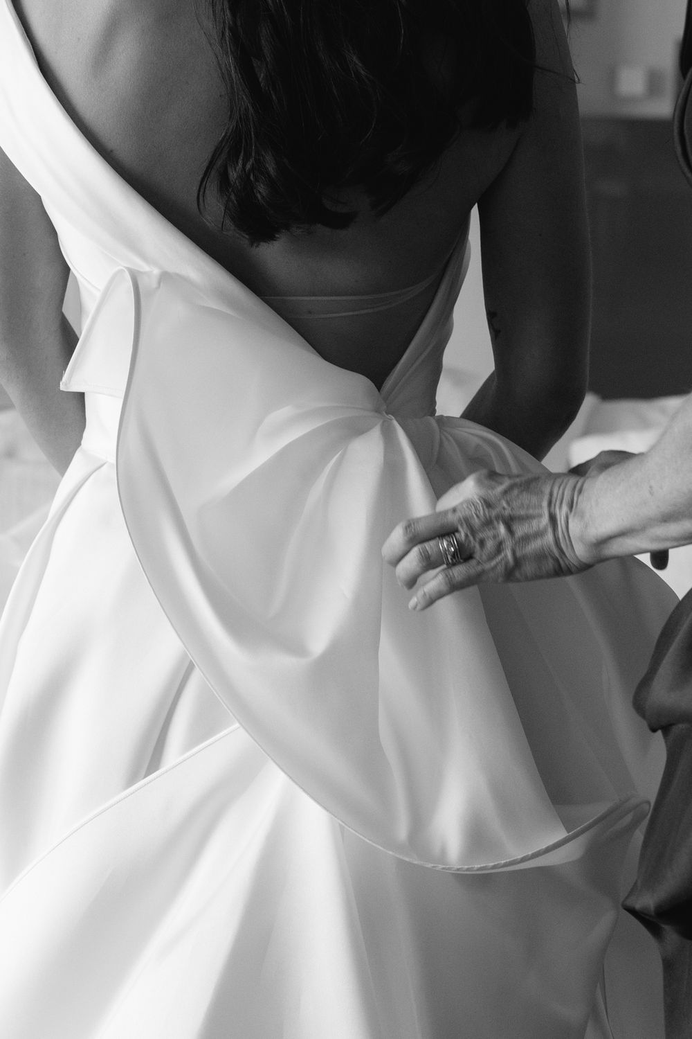 Black and white photo showing someone adjusting a white wedding dress in preparation for a ceremony.
