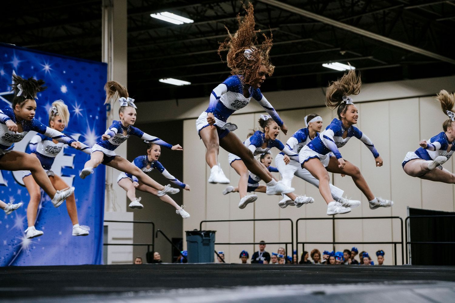 Dynamic sequence of cheerleaders performing synchronized jumps against blue background.