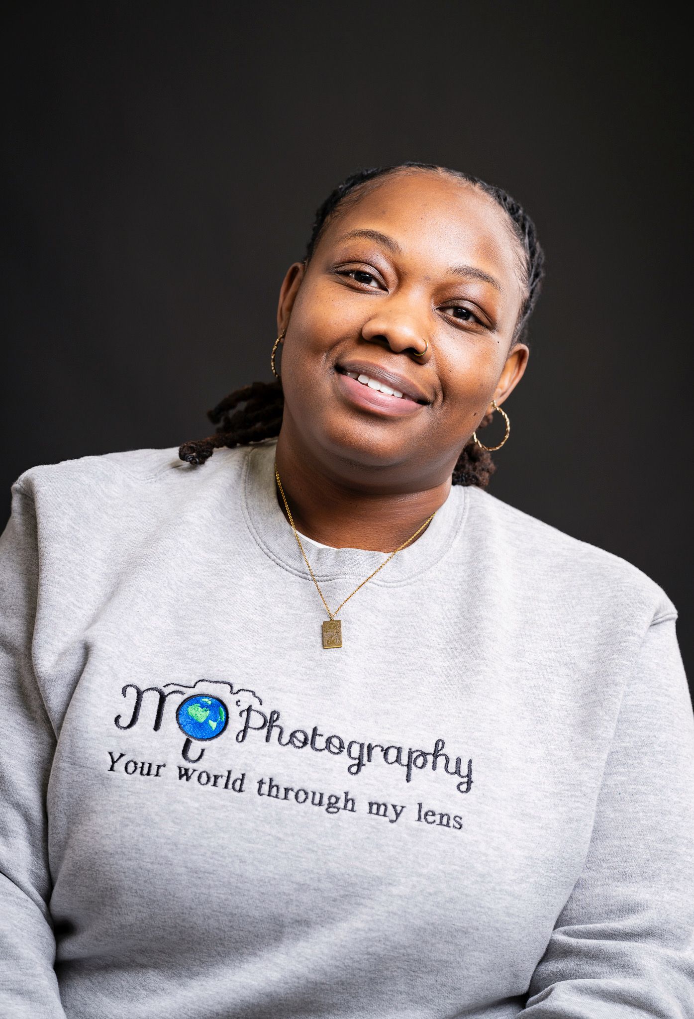 Portrait of photographer wearing branded gray sweatshirt with company logo against dark background.