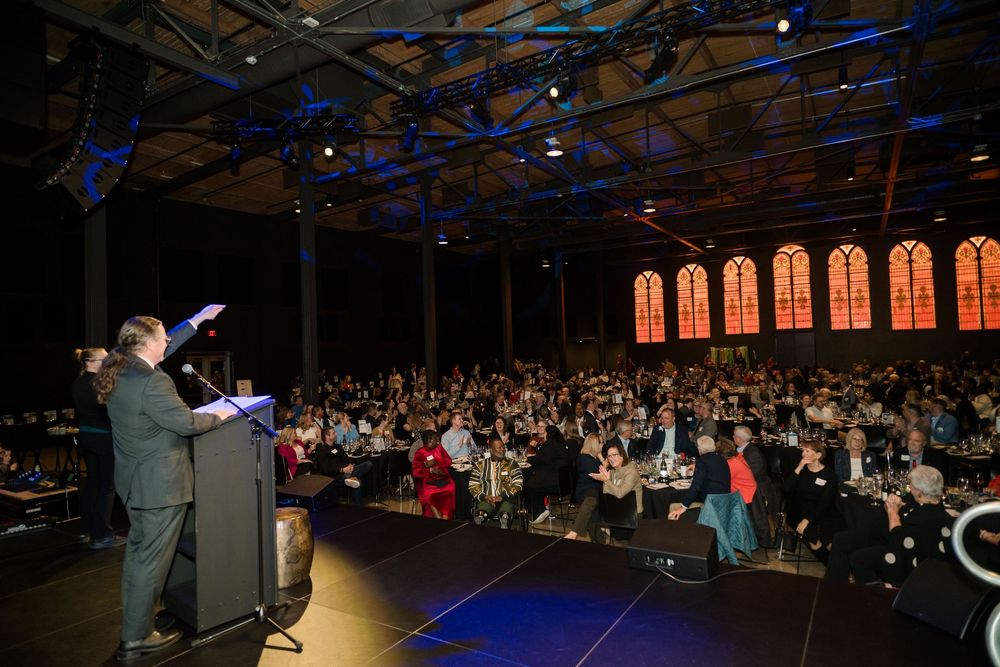 Wide shot of a dimly lit auditorium with rows of attendees during a presentation.